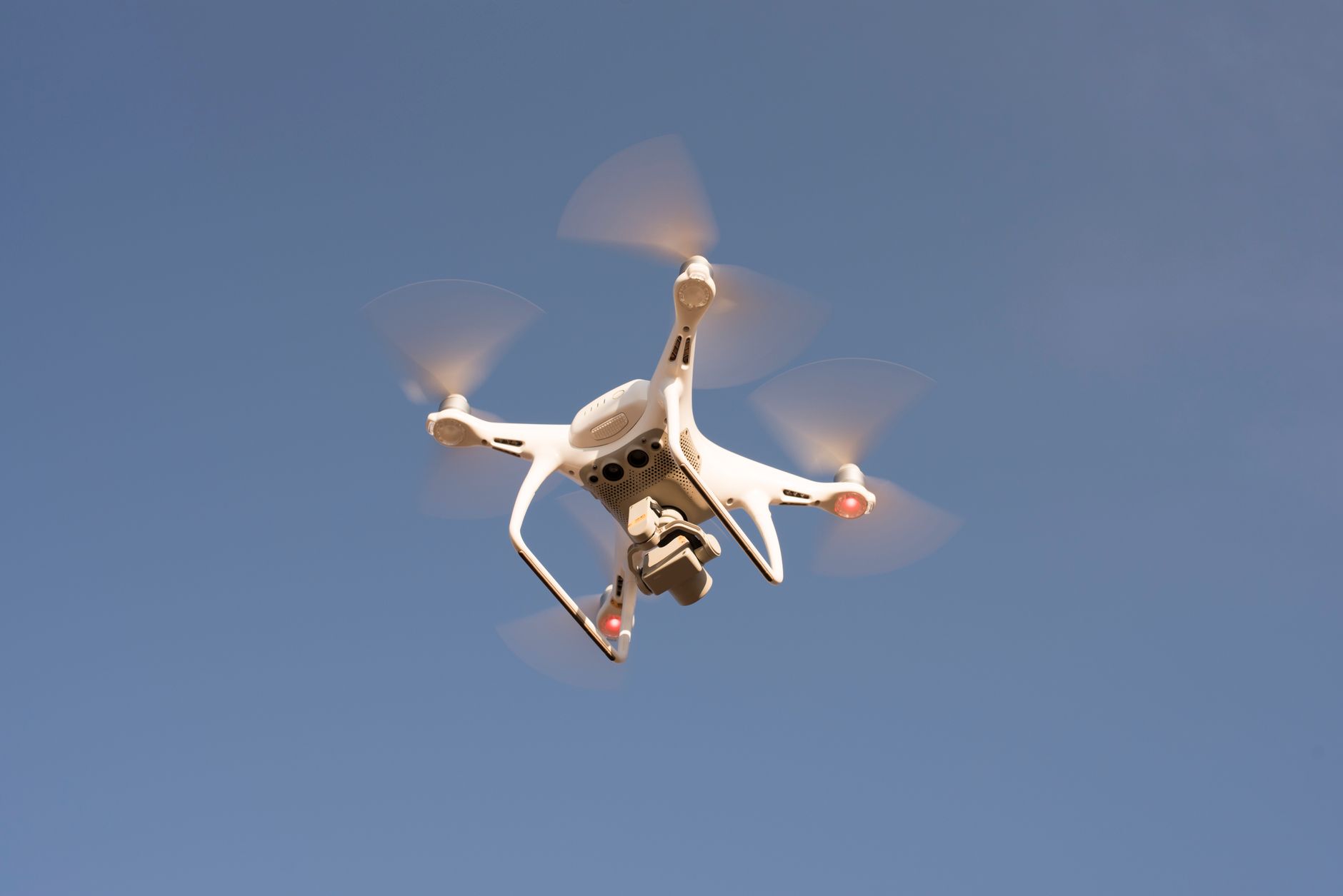 A white drone in flight against a clear blue sky, capturing aerial footage with precision.